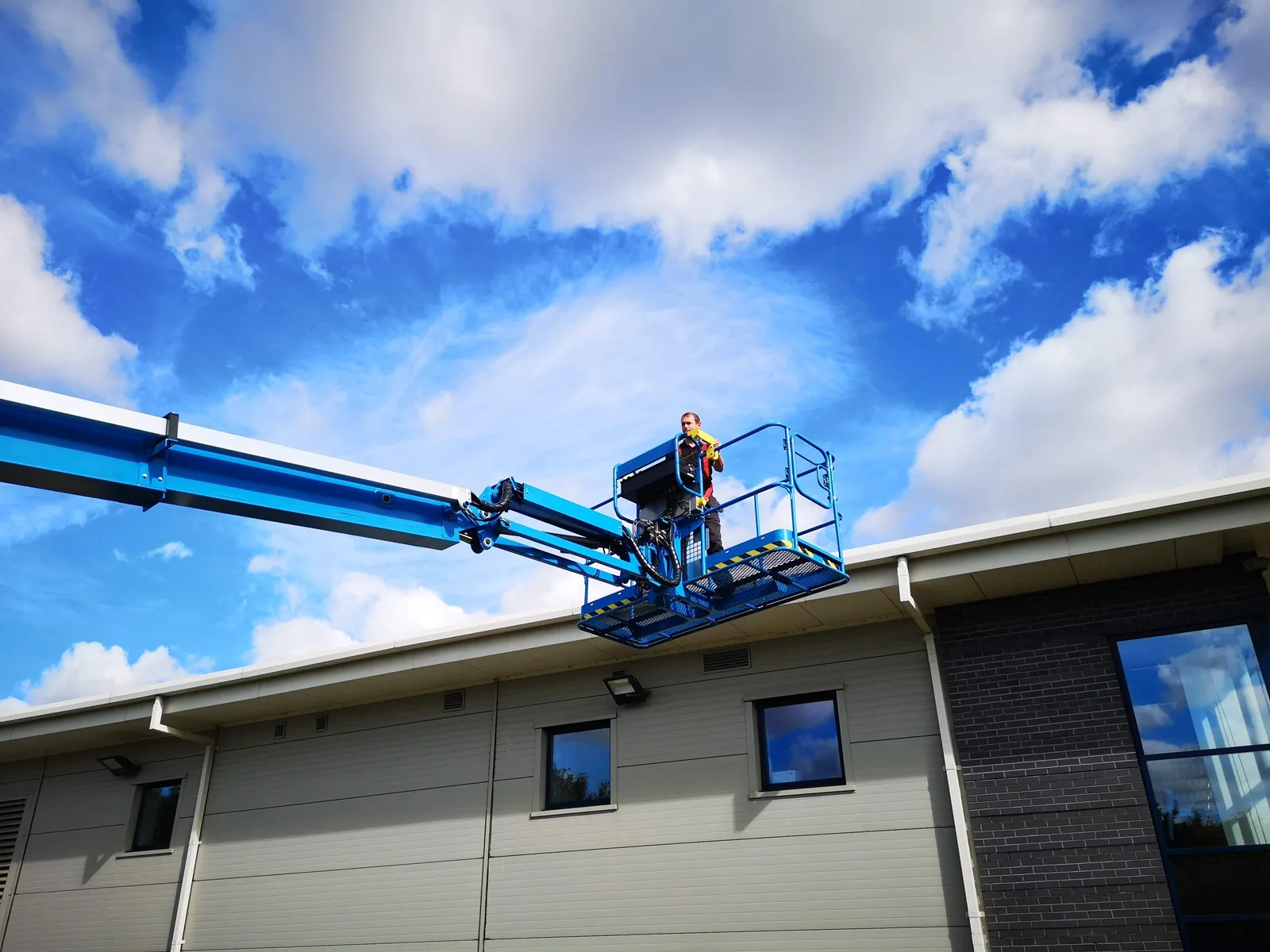 Operative in a cherry picker cleaning at the roofline of a commercial building