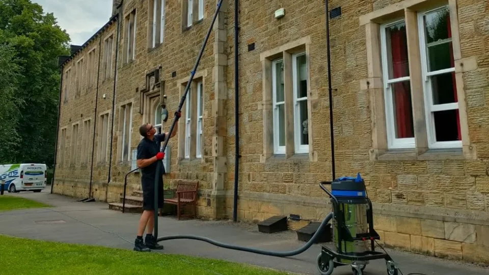 Gutter vacuum clearing the gutters of a stone building from the ground