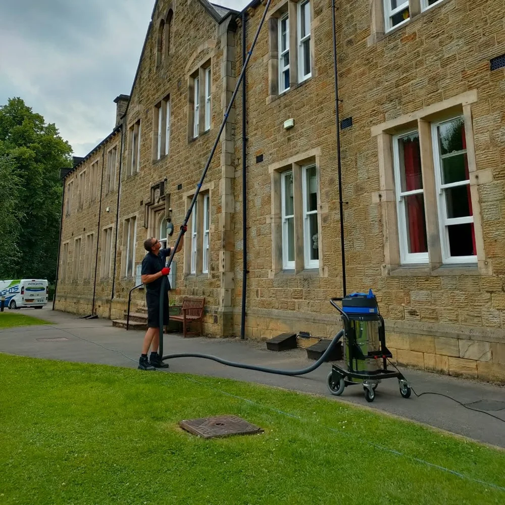 Gutter vacuum clearing the gutters of a stone building from the ground