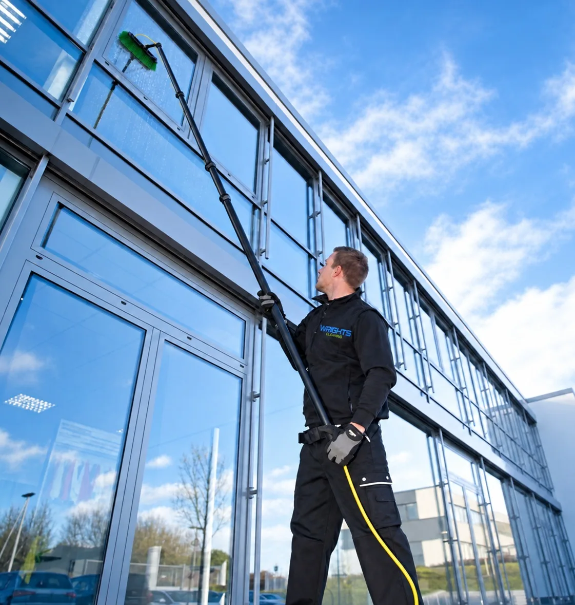 Wrights Cleaning operative cleaning the upper glazing of a modern office with a water-fed pole